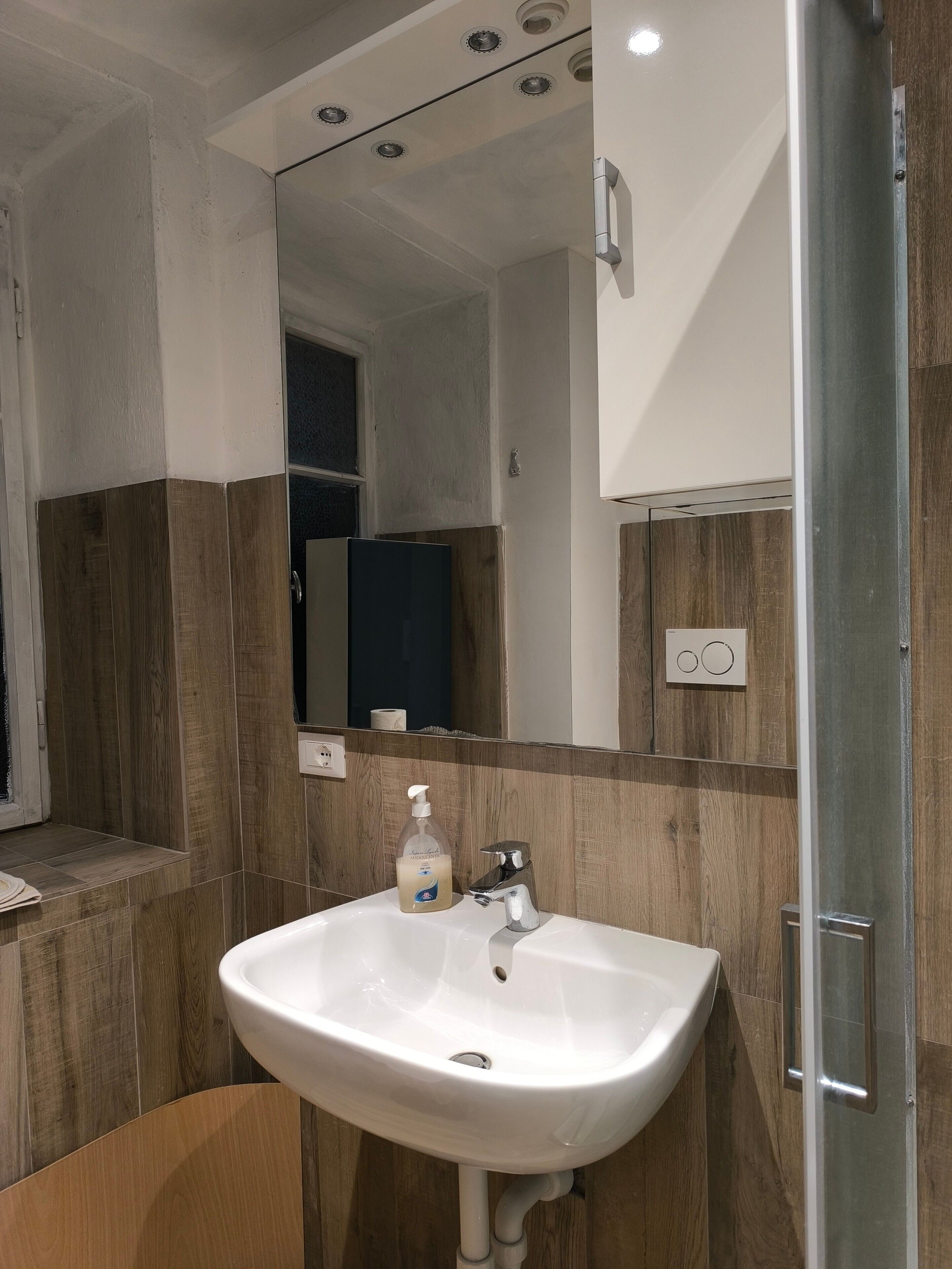 Een badkamer met een wit wastafel, spiegel, houten lambrisering en een douchedeur.
