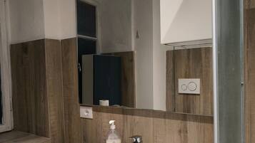 Un baño con un lavamanos blanco, un espejo, paneles de madera y una puerta de ducha.