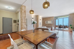 Un vaste espace dédié à la salle à manger, avec une table en bois, des chaises blanches, des murs en pierre et une grande fenêtre offrant une vue panoramique.