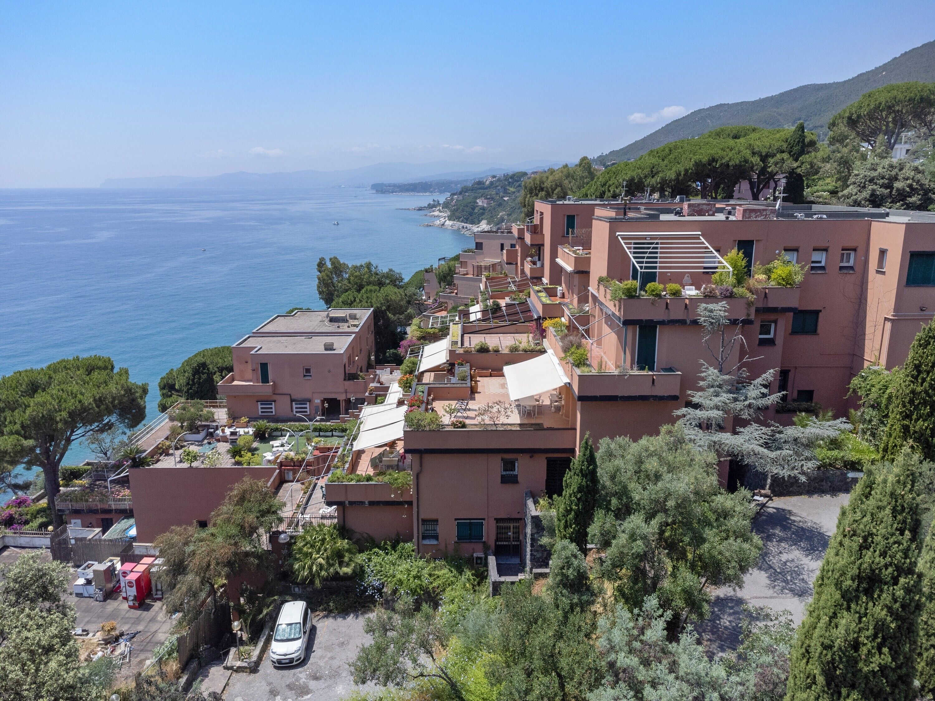 A coastal residential area with buildings, a parked car, and a view of the sea.