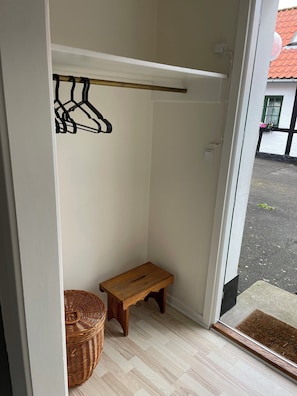 A room with a wooden bench, a wicker basket, a coat rack, and a door leading outside.