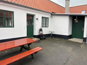 A white building with green doors and windows, a red bench, and a small table.