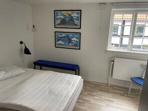 A bedroom with a bed, a bench, two framed posters, a desk, and a window.