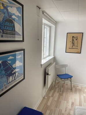 Une pièce avec un radiateur, une fenêtre, une chaise et deux affiches encadrées accrochées au mur.