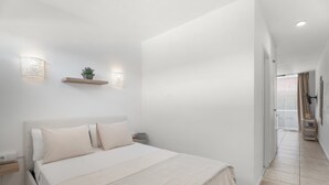 Een slaapkamer met een bed, nachtkastjes, wandlampen, een plank met een plant en uitzicht op de gang.