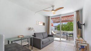 Een moderne woonkamer met een bank, een glazen tafel, een plafondventilator en een balkon met buitenmeubilair.