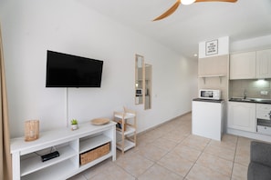 A modern living room with a flat-screen TV, a small plant, and a wooden shelf. - Vacation Studio 'Greta' with Shared Pool, Balcony, and Wi-Fi (Costa del Silencio)