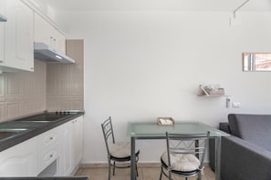 A compact kitchen with white cabinetry, a glass-top table, two chairs, and a grey sofa. - Vacation Studio 'Greta' with Shared Pool, Balcony, and Wi-Fi (Costa del Silencio)