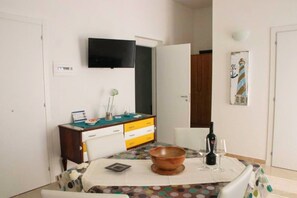 A dining area with a table set for two, a television mounted above the table, and a decorative wall piece.