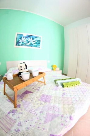 Een slaapkamer met een bed, nachtkastje met lamp, schilderij aan de muur en raam met gordijnen.