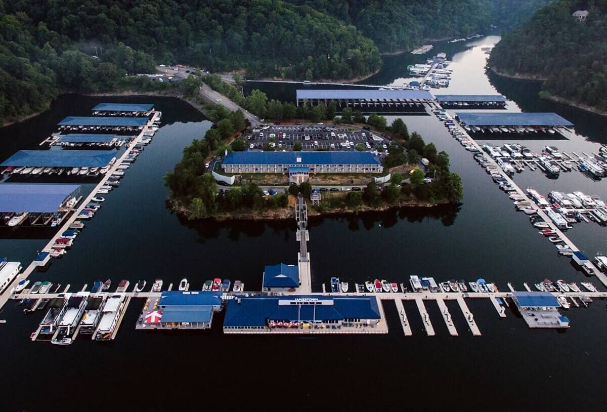 An aerial view of a marina with multiple docks, a central building with a blue roof, and surrounding greenery.