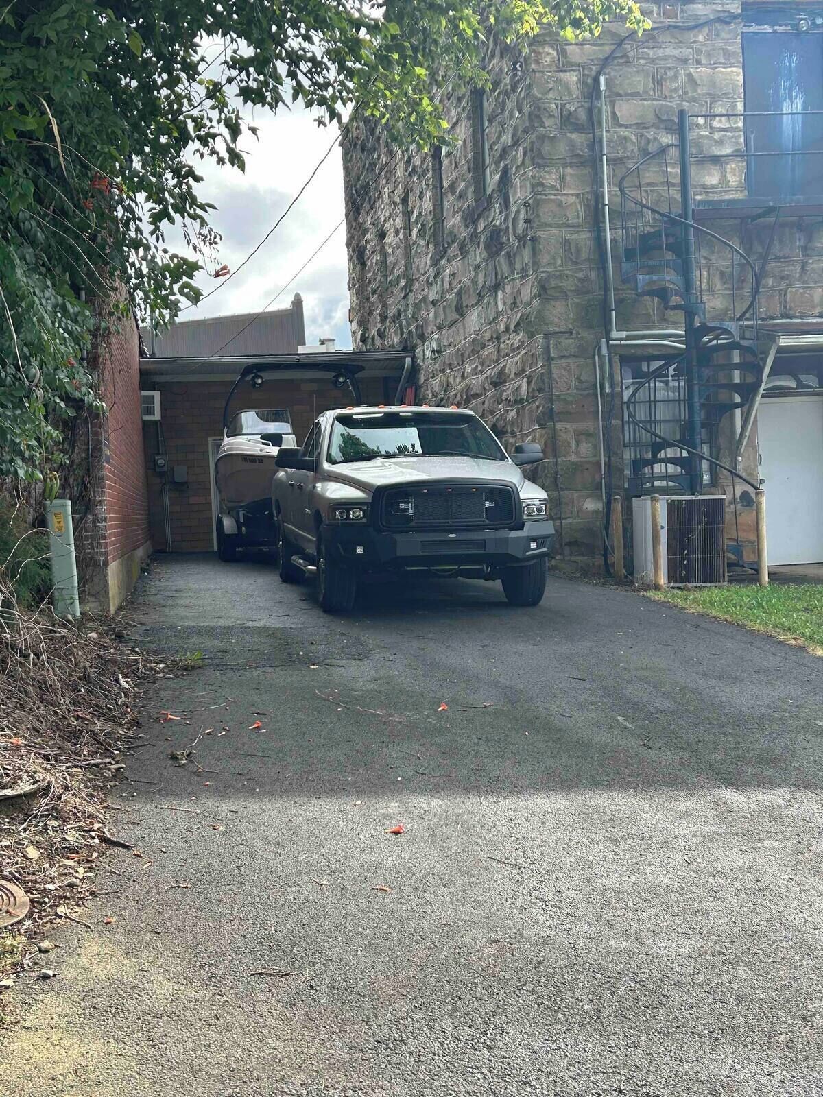 Um veículo estacionado na entrada da garagem, com um muro de pedra e uma escada de metal à direita.