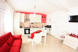 Un ambiente compatto con angolo cottura, zona pranzo e divano rosso.