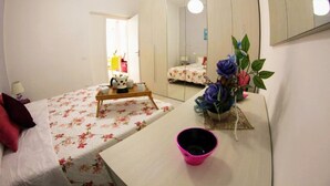 A bedroom with a bed, a dresser, a mirror, and a small table with a cup and a plant.