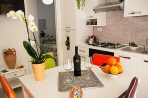 Un'area pranzo con un tavolo apparecchiato per due, una bottiglia di vino e una ciotola di frutta.