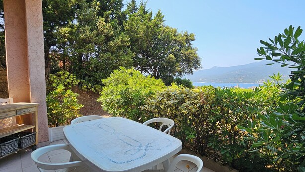 Un patio con mesa y sillas, rodeado de abundante vegetación y vistas al mar.