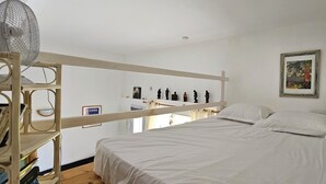 Una habitación con literas, un ventilador, un cuadro enmarcado y una estantería con libros.