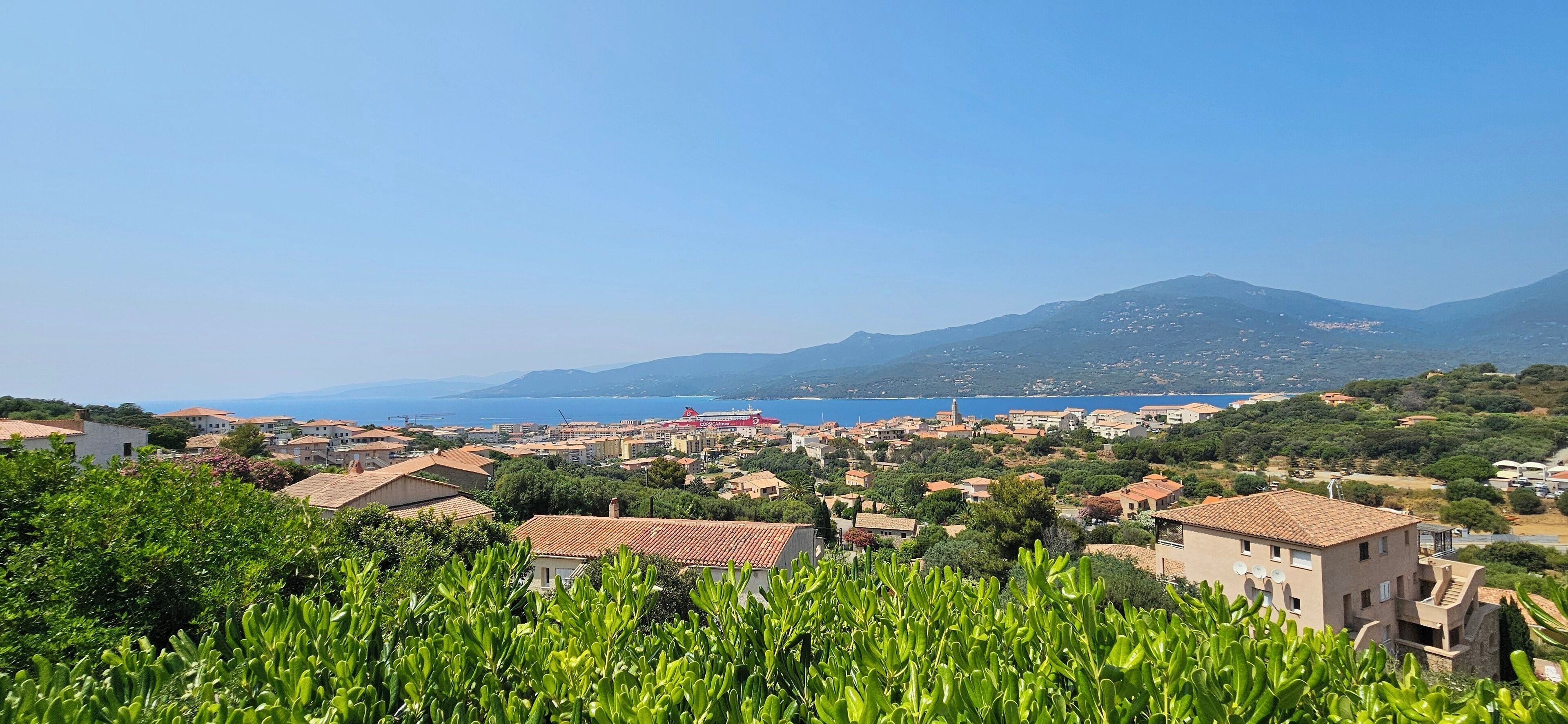 A coastal town with buildings, a mountain, and a clear blue sky.