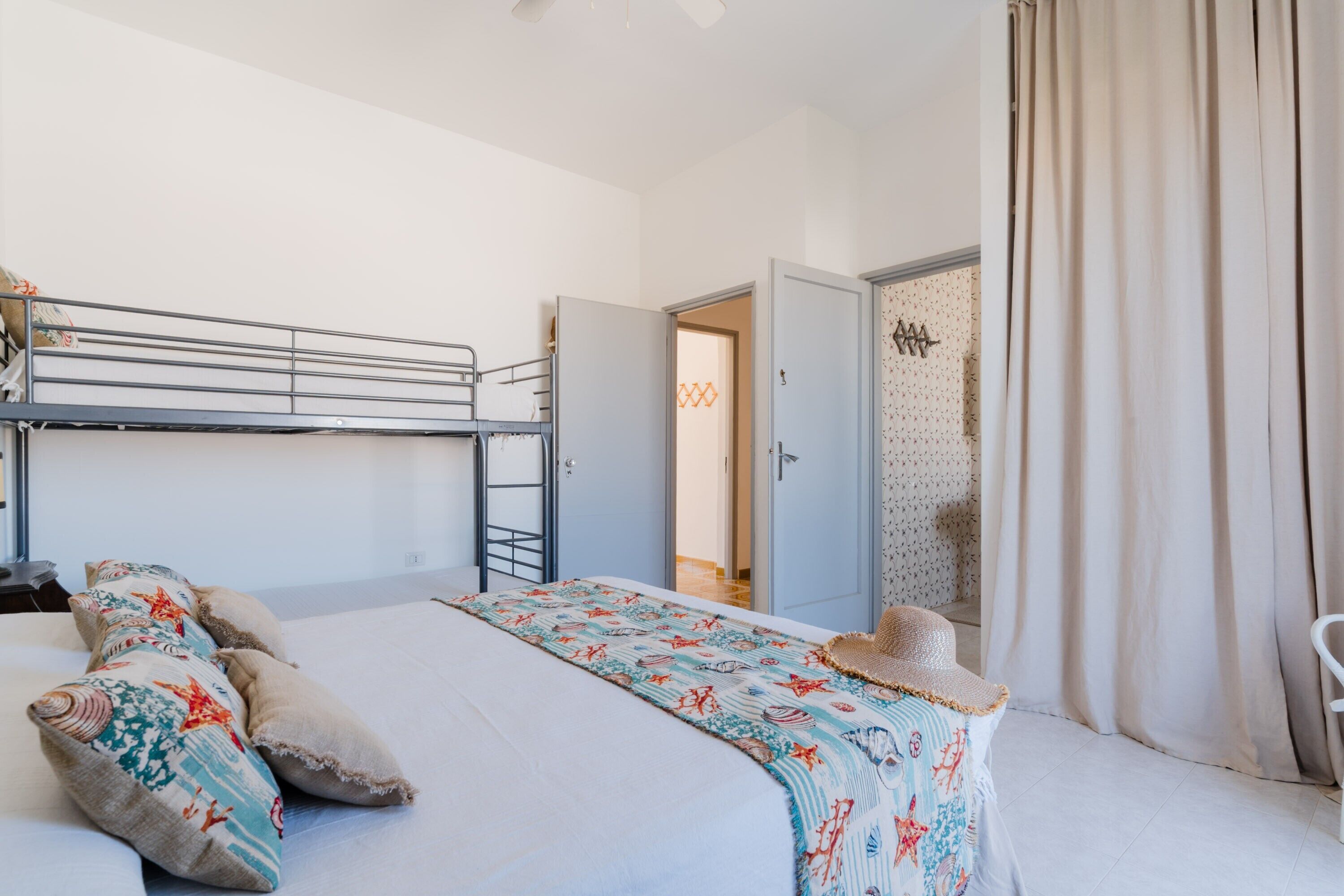 Une chambre avec un lit superposé, une couvre-lit à motifs, des oreillers, un chapeau et une porte donnant sur une autre pièce.