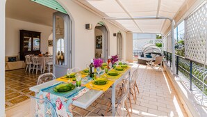 An outdoor dining area with a table set for four, a covered patio, and a view of the garden. - Holiday Home 'Lola' with Private Terrace, Private Garden and Air Conditioning (Porto Cesareo)