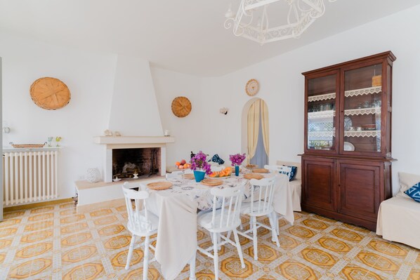 Un coin repas avec une table ronde, des chaises blanches, une cheminée et un buffet aux portes vitrées.