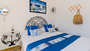 A neatly arranged bedroom with a bed, a wall-mounted picture, a bedside table, and a hanging bag. - Holiday Home 'Lola' with Private Terrace, Private Garden and Air Conditioning (Porto Cesareo)