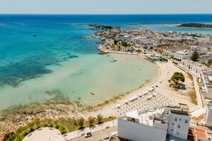 Une vue aérienne d’une ville côtière avec une plage, des bâtiments et une mer bleue et limpide.