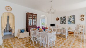 A dining area with a round table, white chairs, and a patterned floor. - Holiday Home 'Lola' with Private Terrace, Private Garden and Air Conditioning (Porto Cesareo)