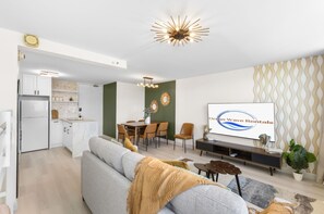 A modern living room with a sofa, TV, dining area, and kitchen.