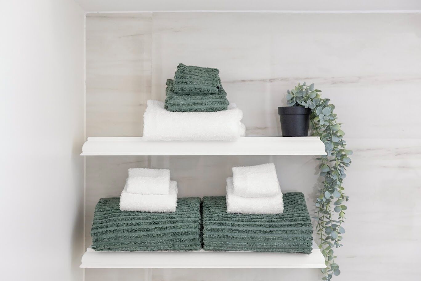 A bathroom with two white shelves, each holding folded towels.