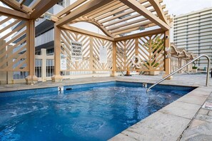 A swimming pool with a wooden pergola structure, a lifeguard sign, and a view of a modern building in the background. - Newly Renovated 1 Bdr Island Colony for 6, 7 Minutes to Beach (Honolulu)