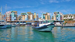 A marina with boats docked, a colorful building complex in the background, and clear blue skies.