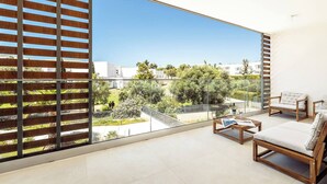 A modern living room with a large balcony, wooden blinds, and a view of a residential area.