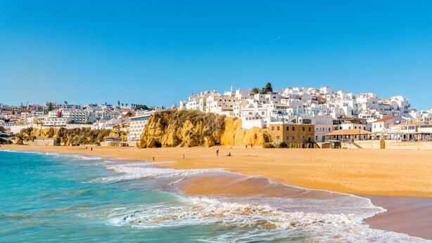 A coastal town with white buildings, a sandy beach, and waves.