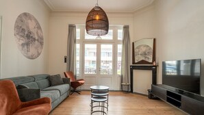 A living room with a grey sofa, a brown armchair, a round coffee table, a TV, and a fireplace.