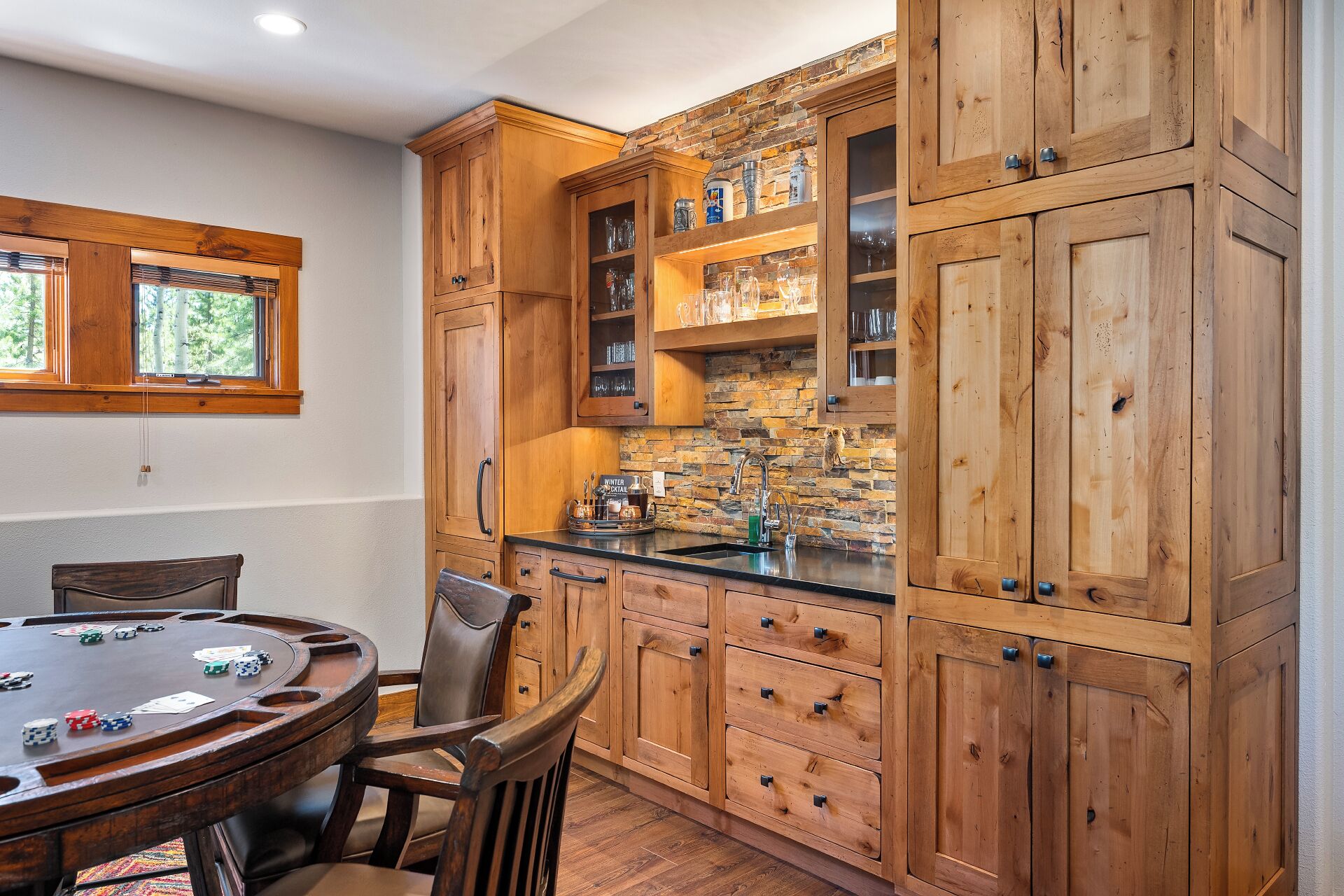 Una cocina de madera con salpicadero de piedra, una mesa de comedor con sillas y una mesa de póker.