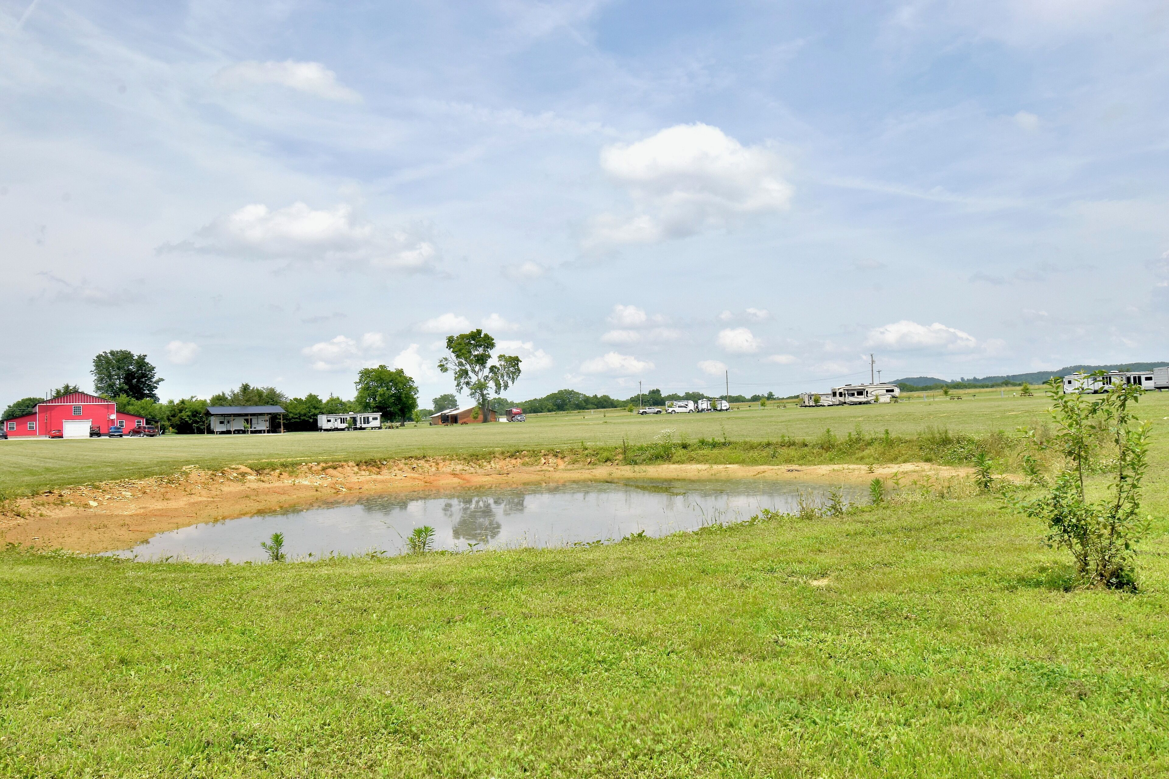 A rural landscape with a pond, green fields, and several buildings including a red barn and a white house.