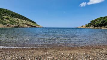 A pebbled beach with clear water and hills in the background.