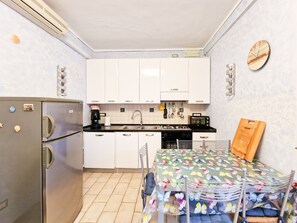 Una cocina compacta con gabinetes blancos, un refrigerador de acero inoxidable, una cafetera, un tostador y una mesa de comedor con mantel floreado.