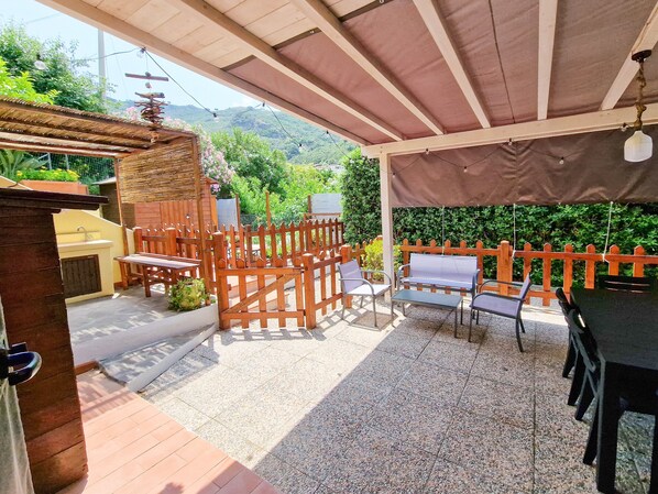 An outdoor patio with a wooden fence, seating, and a view of greenery and hills.