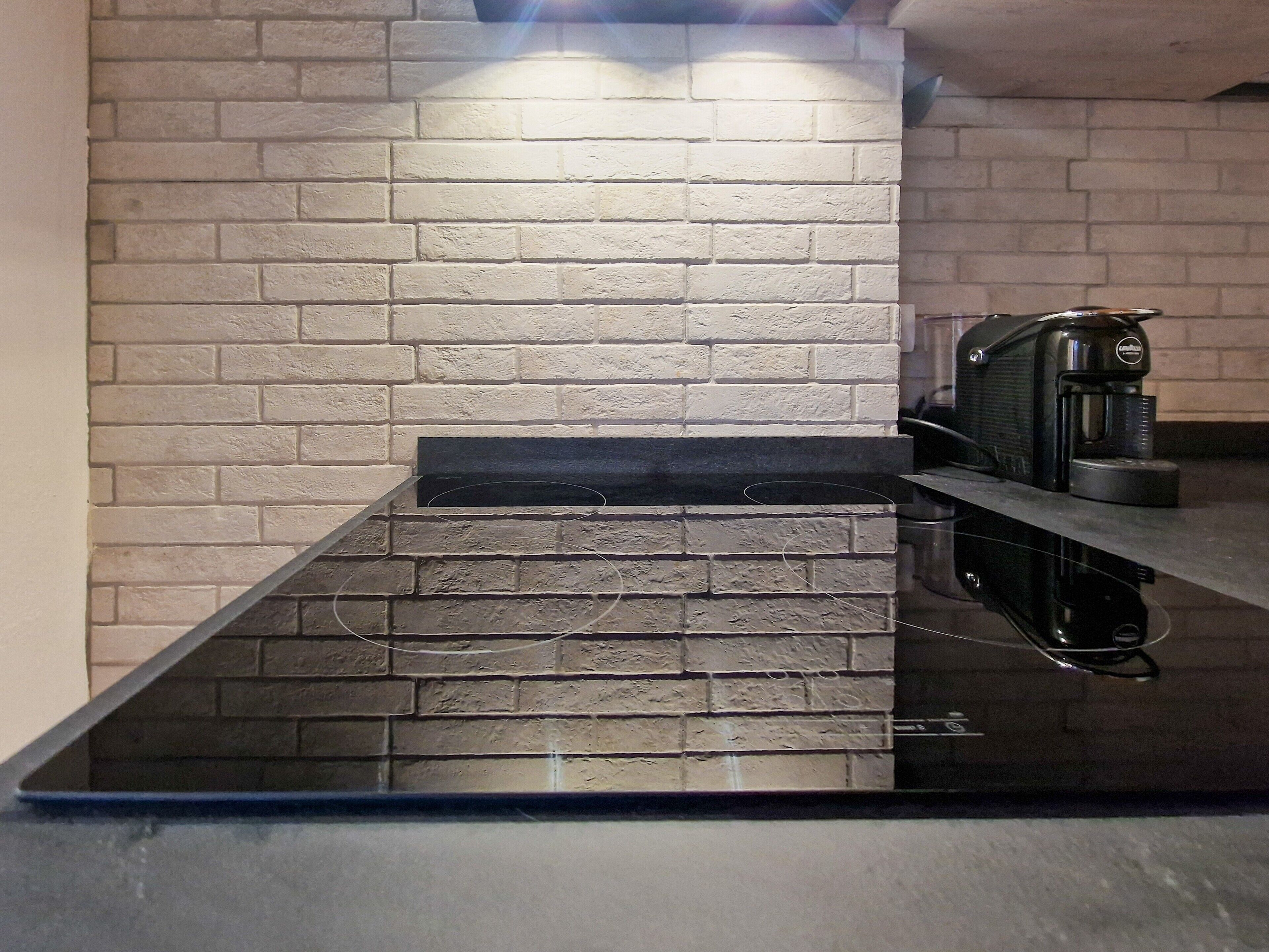 A kitchen with a black countertop, a coffee machine, and a brick wall.