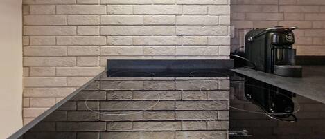 A kitchen with a black countertop, a coffee machine, and a brick wall.