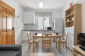 A modern kitchen with wooden cabinets, a dining table with chairs, a refrigerator, and a TV on a stand.