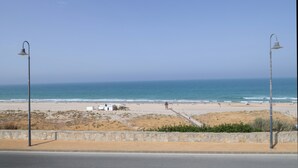 A beach with a stone wall, a road, and two street lamps.