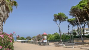 A paved walkway, a playground with a red-roofed structure, and trees.