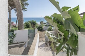 A pathway leading to a balcony overlooking a beach, with tropical plants and a white wall. - 'Mirador De La Atalaya' Apartment with Sea View, Private Terrace, Garden & Wi-Fi (Conil de la Frontera)