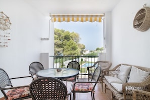 A balcony with wicker furniture, a glass table, and a view of trees and a swimming pool.