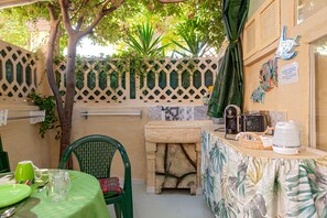 A patio area with a table set for dining, a chair, a small stone structure, and a wall with decorative elements.
