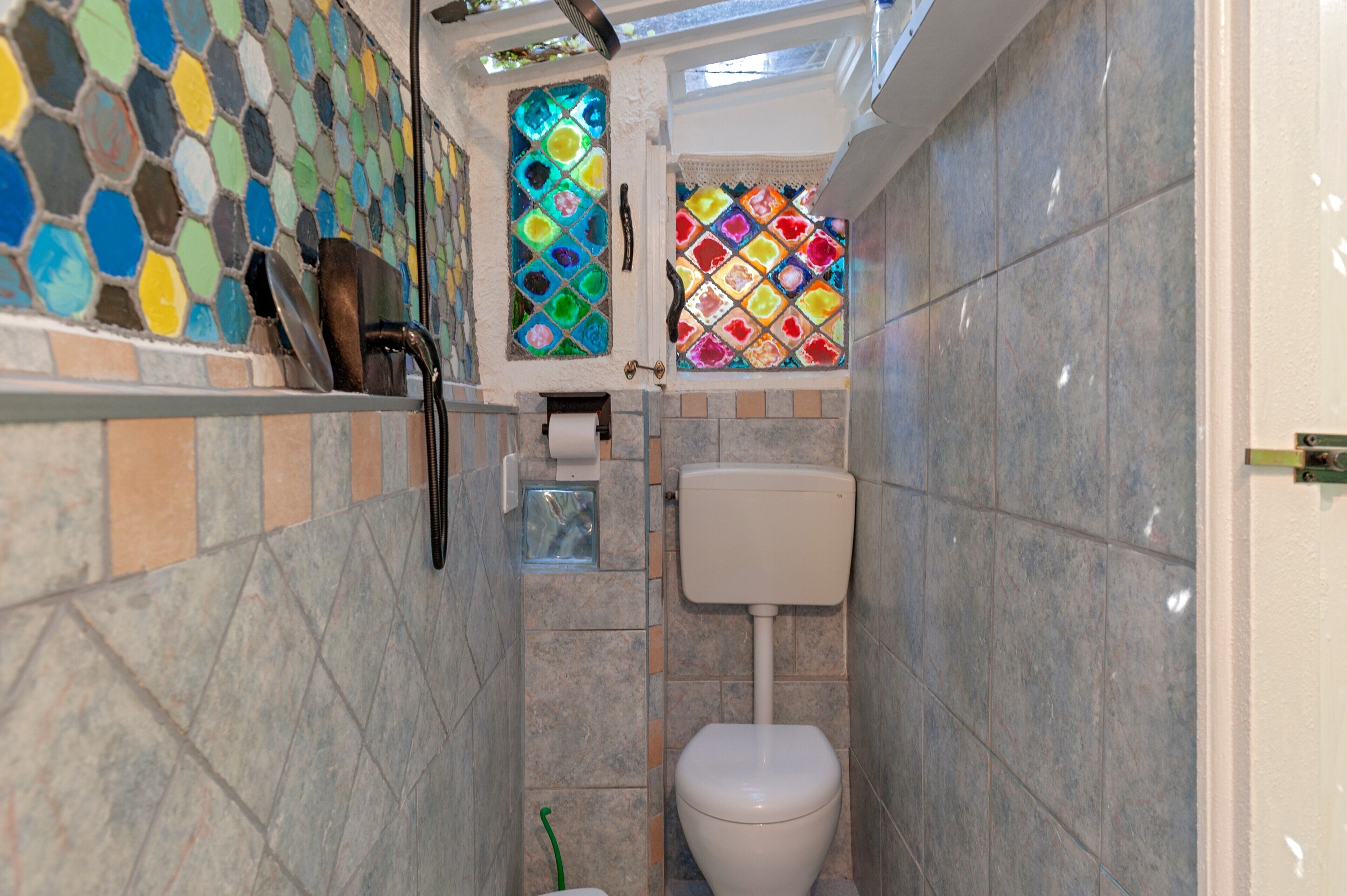 Un baño con suelo de baldosas, inodoro, zona de ducha y pared de mosaico.