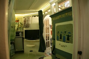 Una habitación pequeña con televisión, una mesita y una puerta con un panel decorativo.